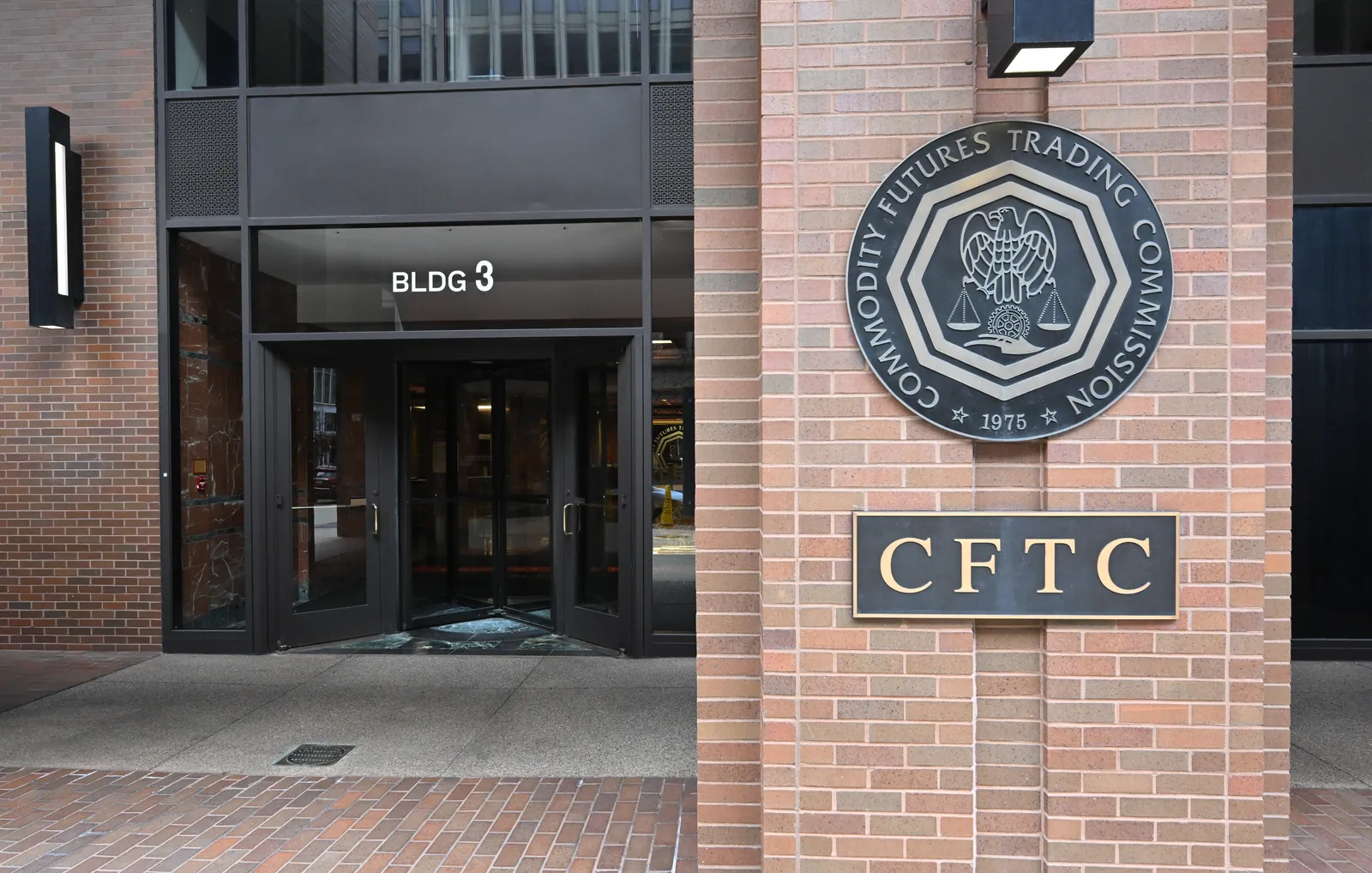 The entrance to the Commodity Futures Trading Commission at Three Lafayette Centre, Washington, DC, with the Commission's seal and CFTC sign on the brick wall.