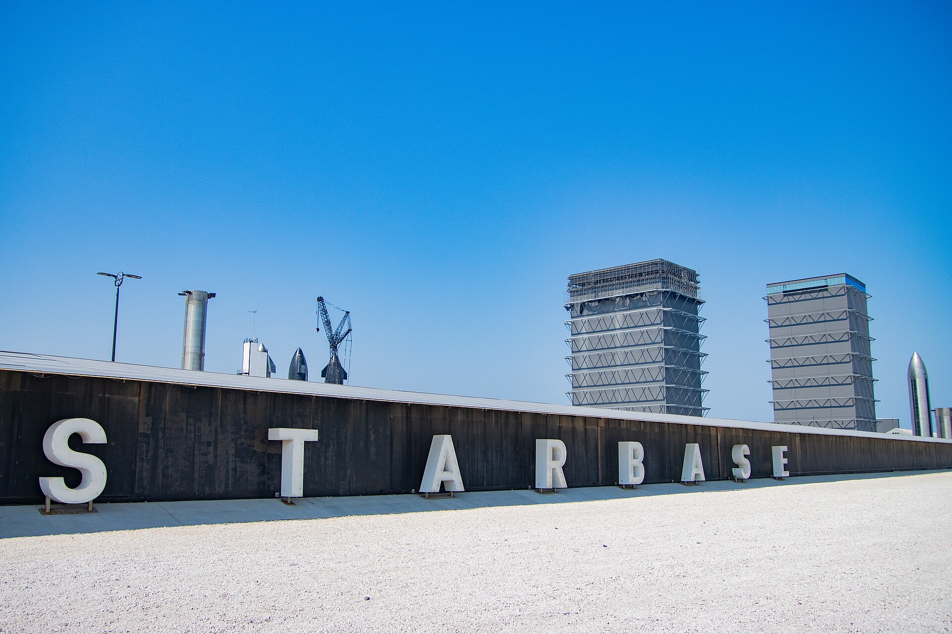 The Starbase sign beside Texas State Highway 4, with Starship boosters and vehicles on the horizon.